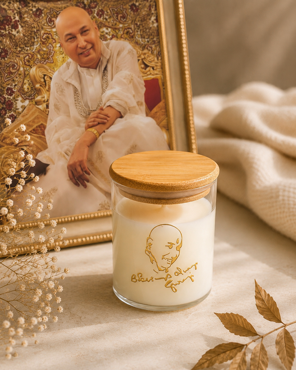 Guruji's Blessing candle lit beside a framed photo of Guruji, gold-engraved glass jar